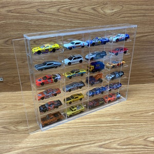 May include: A clear acrylic display case with multiple shelves for storing and displaying toy cars. The case is filled with a variety of colorful toy cars, including red, blue, yellow, and black cars.