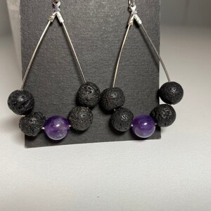 May include: A pair of silver dangle earrings with black lava rock and amethyst beads. The earrings are shaped like a teardrop.