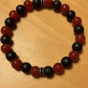 May include: A bracelet made of black and red beads. The beads are round and have a smooth finish. The bracelet is closed with a silver clasp.
