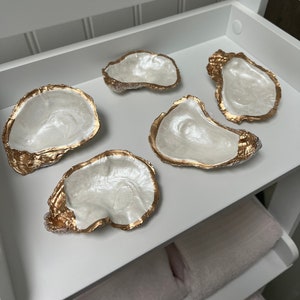 May include: Five white oyster shell dishes with gold accents. The dishes are arranged on a white shelf.