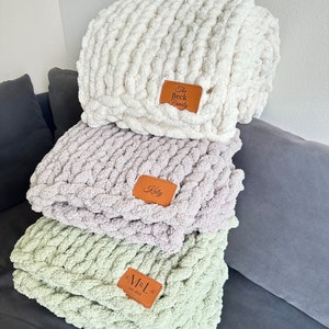 Puede incluir: Tres mantas de punto grueso en crema, lavanda y verde salvia apiladas. Cada manta tiene un parche de cuero marr&oacute;n con texto personalizado: "The Beck Family", "Koty" y "M&L Est. 2022".