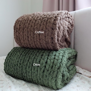 Puede incluir: Dos mantas de punto grueso, una marr&oacute;n caf&eacute; y otra verde oliva, est&aacute;n apiladas sobre una cama. Las mantas est&aacute;n dobladas y parecen suaves y acogedoras. La palabra "Coffee" es visible en la manta superior, y "Olive" en la inferior.