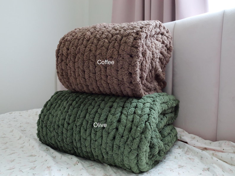 Puede incluir: Dos mantas de punto grueso, una marr&oacute;n caf&eacute; y otra verde oliva, est&aacute;n apiladas sobre una cama. Las mantas est&aacute;n dobladas y parecen suaves y acogedoras. La palabra "Coffee" es visible en la manta superior, y "Olive" en la inferior.
