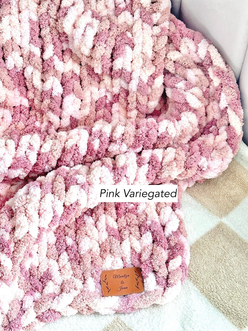 Puede incluir: Una manta de punto grueso en un esquema de color rosa variado. La manta presenta una mezcla de tonos rosas claros y oscuros, creando una apariencia texturizada. Una peque&ntilde;a etiqueta de cuero marr&oacute;n con el texto "Maritza & Joan" est&aacute; adjunta.