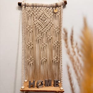 May include: A macrame wall hanging with a geometric design and a wooden shelf with the word "HOME" spelled out in concrete letters.