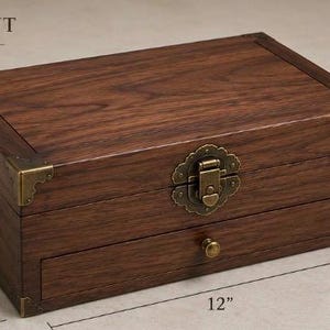 May include: A rectangular walnut storage box with a hinged lid, a front drawer, and brass-toned metal corner accents. The box features a central latch and side handles, with dimensions labeled as 12 inches long, 8 inches wide, and 4 inches high.