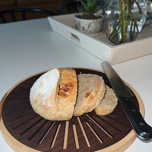 May include: A wooden cutting board with a sunburst design, featuring a loaf of sliced sourdough bread and a black handled knife.
