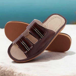 May include: Brown leather sandals with two adjustable straps and a light-colored insole. The sandals have a rubber sole and are designed for comfort. The sandals are approximately 10 inches long.
