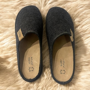 Puede incluir: Un par de zapatillas de lana grises con una plantilla de cuero marr&oacute;n. La plantilla est&aacute; etiquetada como "100% natural".