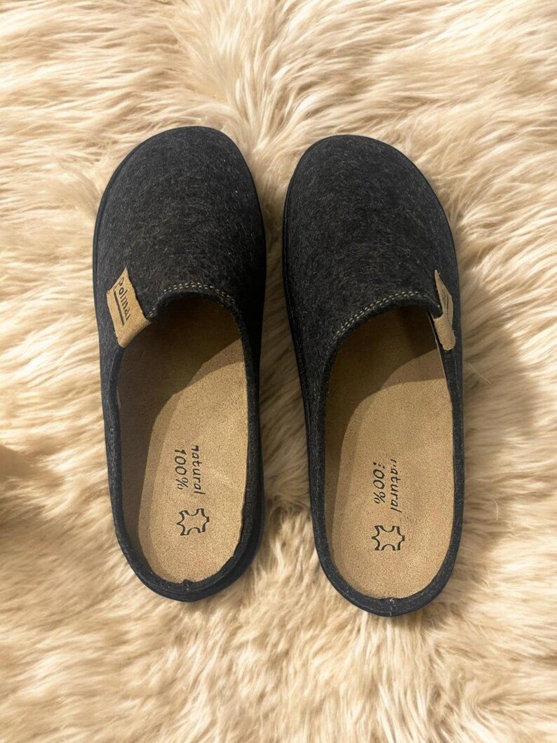 Puede incluir: Un par de zapatillas de lana grises con una plantilla de cuero marr&oacute;n. La plantilla est&aacute; etiquetada como "100% natural".