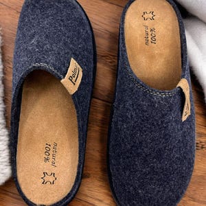 Puede incluir: Un par de zapatillas de lana azul oscuro con una plantilla de cuero marr&oacute;n. La plantilla est&aacute; etiquetada como "100% natural" y "Polmar".