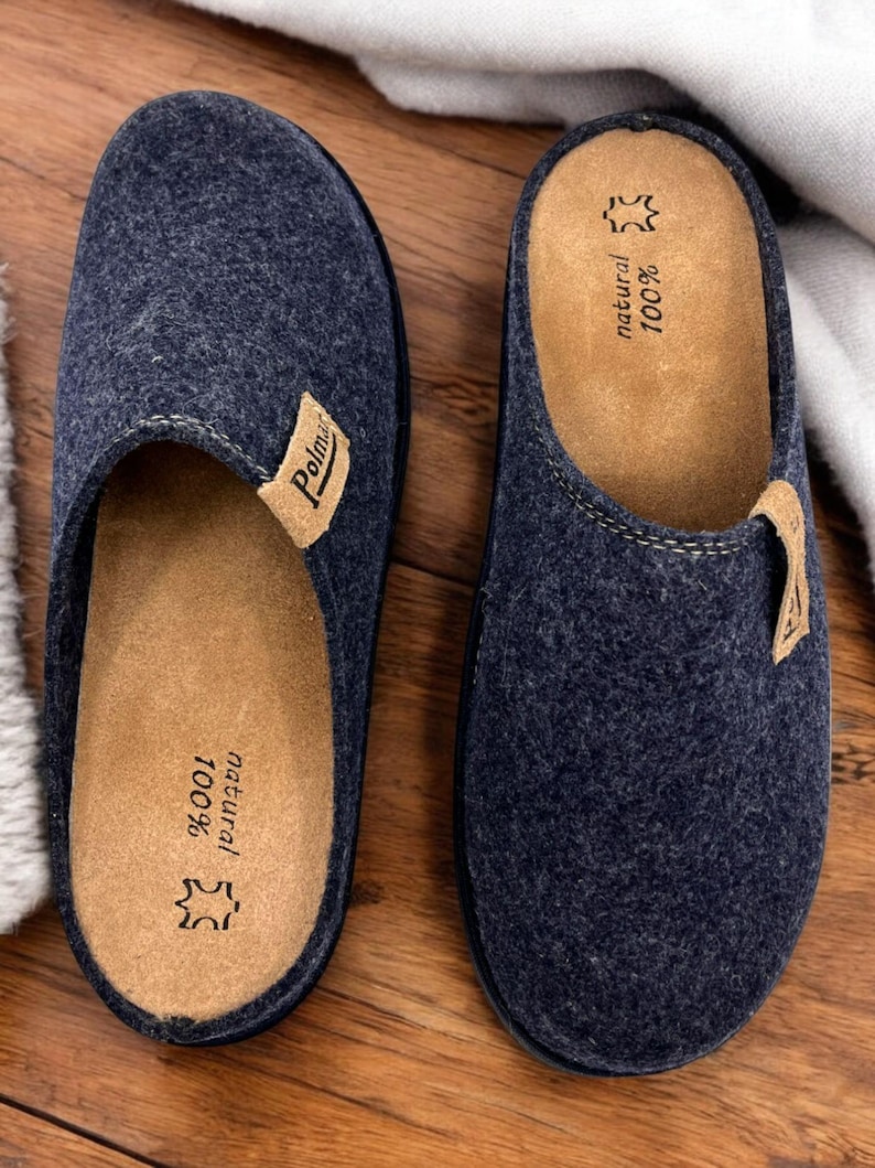 Puede incluir: Un par de zapatillas de lana azul oscuro con una plantilla de cuero marr&oacute;n. La plantilla est&aacute; etiquetada como "100% natural" y "Polmar".