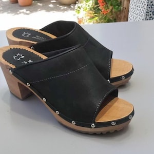 May include: A pair of black leather clogs with a wooden platform and a studded trim. The clogs have an open toe design and a back strap.