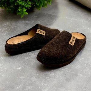 Puede incluir: Un par de zapatillas de lana marr&oacute;n con suela de cuero. Las zapatillas tienen una etiqueta de cuero marr&oacute;n con la palabra "Polmar" en ellas.
