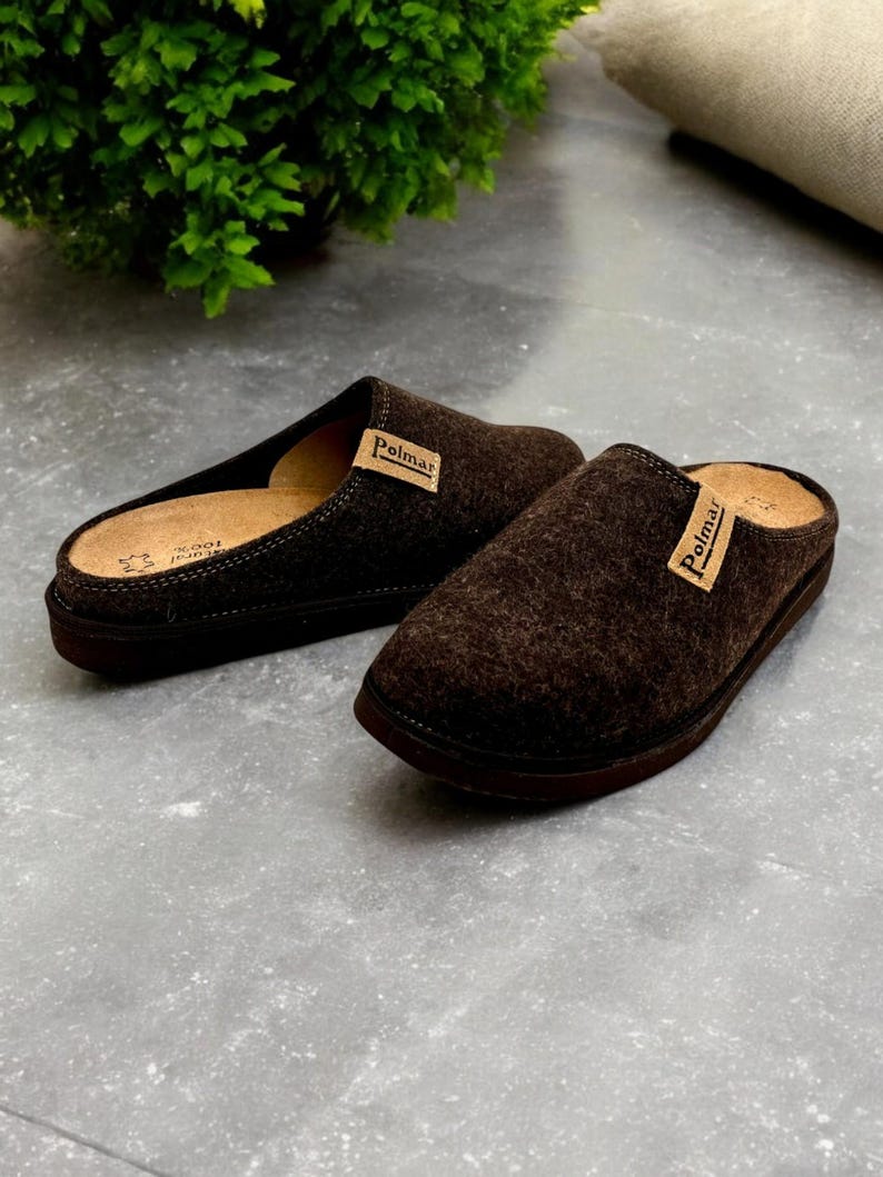 Puede incluir: Un par de zapatillas de lana marr&oacute;n con suela de cuero. Las zapatillas tienen una etiqueta de cuero marr&oacute;n con la palabra "Polmar" en ellas.