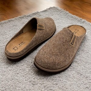 Puede incluir: Un par de zapatillas de fieltro marr&oacute;n con suela negra. Las zapatillas tienen la palabra "Polmar" impresa en la parte superior.