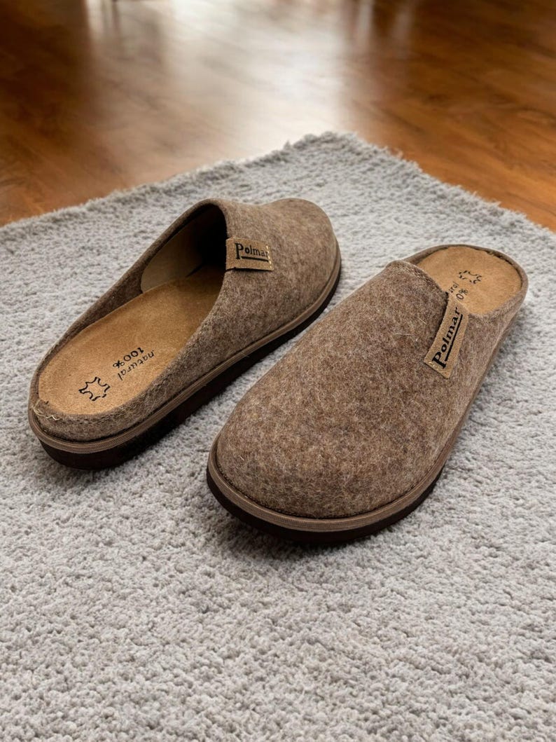 Puede incluir: Un par de zapatillas de fieltro marr&oacute;n con suela negra. Las zapatillas tienen la palabra "Polmar" impresa en la parte superior.