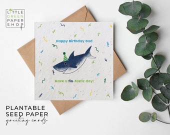 Può includere: Biglietto di auguri in carta da seme piantabile con uno squalo blu che indossa un cappello da festa verde. La carta dice "Buon compleanno papà" e "Have a fin-tastic day!"