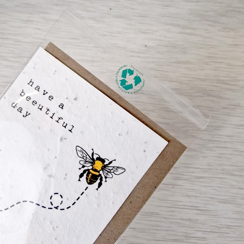 May include: A white card with the text "have a beautiful day" and a black and yellow bee with a dotted line behind it. The card is in a clear plastic sleeve with a green recycling logo.