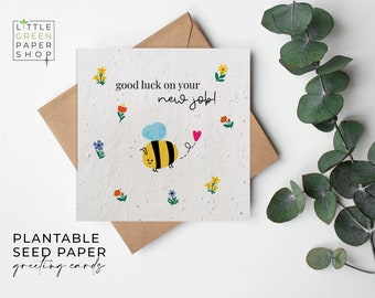 May include: A white plantable seed paper greeting card with a bee illustration and the text "good luck on your new job!" The card is surrounded by small flower illustrations.