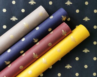 May include: Four rolls of wrapping paper with a honeycomb and bee pattern. The rolls are in different colors: beige, navy blue, burgundy, and yellow.