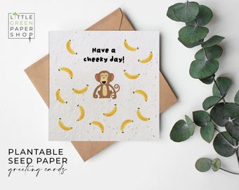 May include: A white card with a monkey illustration and the text "Have a cheeky day!" surrounded by yellow bananas. The card is made of plantable seed paper and has the text "Plantable Seed Paper greeting cards" at the bottom.