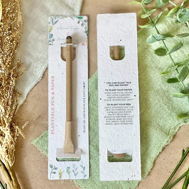 May include: A white card with green floral designs and the text "Plantable Pen & Paper" and "Plant me and watch our love grow!"  The card has a brown wooden pen with a seed capsule at the end. The back of the card has instructions on how to plant the pen and paper.