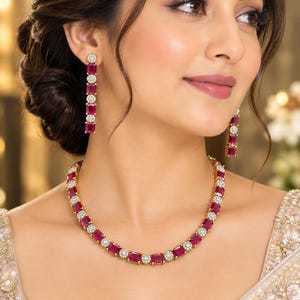 May include: A gold necklace and matching drop earrings featuring alternating rectangular magenta-coloured gemstones and small circular white stones. The necklace is a continuous strand of these stones, while the earrings consist of three segments.