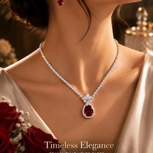 May include: A silver-toned necklace featuring a continuous row of clear stones and a central pear-shaped red stone pendant surrounded by small clear stones. Matching star-shaped earrings with red pear-shaped drops are worn. Text reads: Timeless Elegance.