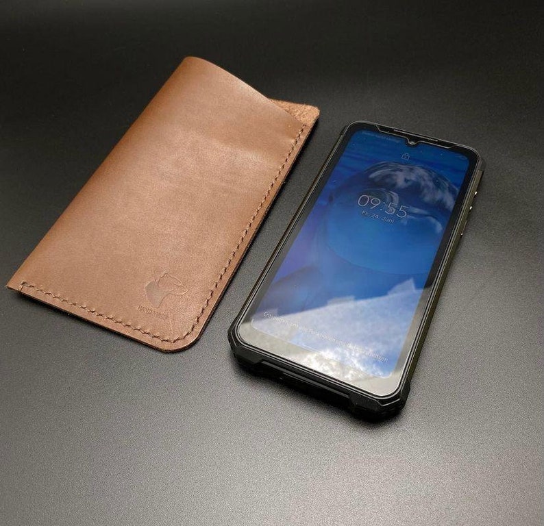 May include: A brown leather phone case with a stitched edge and a small bear logo. A black rugged phone case with a screen protector is next to it. The phone screen shows the time 09:55.