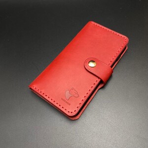 May include: A red leather phone case with a gold button and the words "HAND MADE" embossed on the front.
