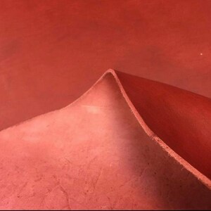 May include: Close-up of a folded piece of red leather. The leather has a textured surface and a slightly darker red hue on the folded edge.