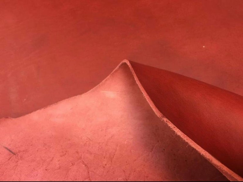May include: Close-up of a folded piece of red leather. The leather has a textured surface and a slightly darker red hue on the folded edge.