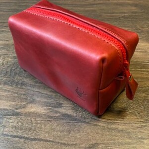 May include: A red leather zippered pouch with a small logo on the front.