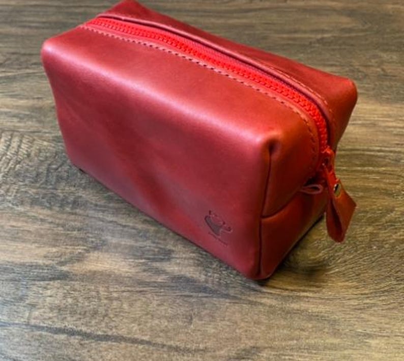 May include: A red leather zippered pouch with a small logo on the front.