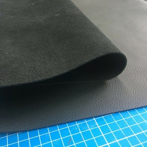 Pode incluir: Duas peças de couro preto, uma lisa e outra de camurça, estão dobradas uma sobre a outra. O couro está sobre um tapete de corte azul.
