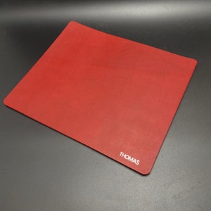 May include: Red leather desk mat with the word "THOMAS" embossed in white lettering.