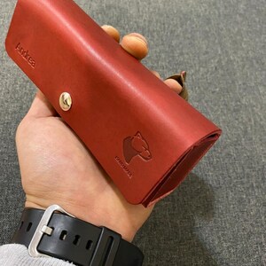 May include: A red leather case with the name "Andrea" embossed on the front. The case has a snap closure and a small bear logo with the word "Handmade" underneath.