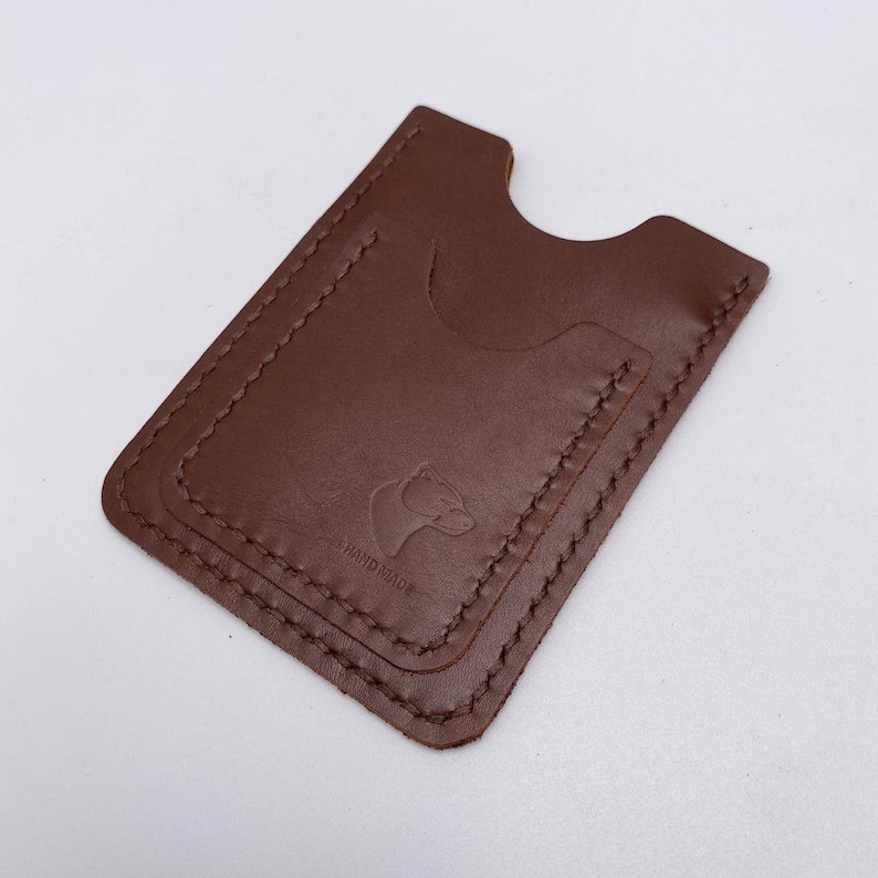 May include: A brown leather card holder with a stitched edge and a small bear logo that says "HAND MADE".