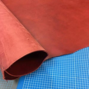 Pode incluir: Close-up de um pedaço de couro vermelho enrolado em um tapete de corte azul. O couro é liso e tem um leve brilho.