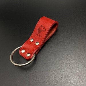 May include: Red leather belt loop with a silver ring and a bear head logo that says "Hand Made".