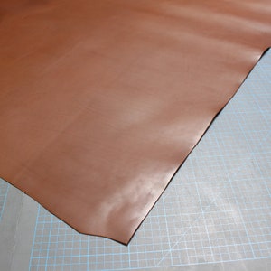 May include: A piece of brown leather on a cutting mat.