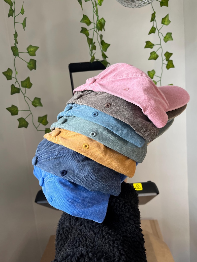 Op de afbeelding: Stapel van zes baseballpetten in verschillende kleuren, waaronder roze, bruin, teal, geel, blauw en lichtblauw. De petten zijn gemaakt van een zachte, textuurrijke stof.