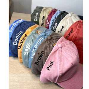 Op de afbeelding: Een verzameling van 14 baseballpetten in verschillende kleuren, waaronder korenbloemblauw, denim, mosterd, salie, lichtblauw, bruin, olijf, steen, rood, zwart, lichtblauw, zand, roze en oranje.