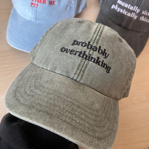 Op de afbeelding: Een groene baseballpet met de tekst "probably overthinking" geborduurd in het zwart op de voorkant.