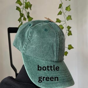 May include: A bottle green baseball cap with a curved brim. The cap is made of a soft, textured fabric.