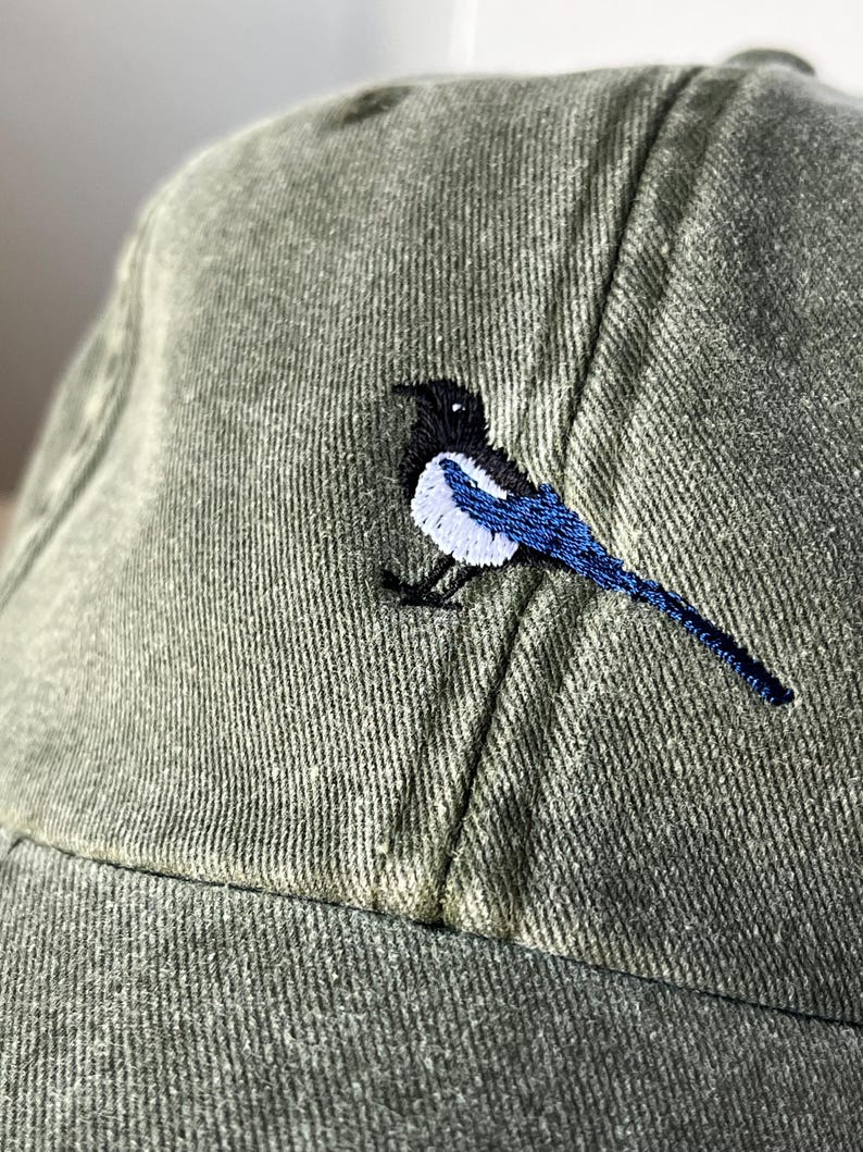 May include: A green baseball cap with an embroidered black and white magpie with blue wings.