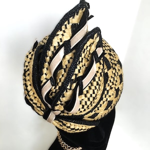 May include: A woven hat featuring a black and tan checkered design, with black edging and beige ribbon detailing. The hat is presented on a black mannequin head, adorned with a gold chain necklace. The hat's construction is detailed and striking.