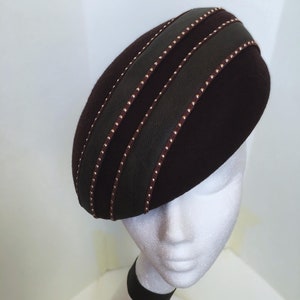 Peut inclure: Un béret en feutre bordeaux avec un bandeau en cuir noir et des clous dorés. Le bandeau comporte trois rangées de clous.