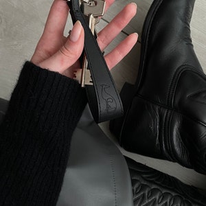 Puede incluir: Llavero de cuero negro con una llave plateada y un pequeño anillo plateado. El llavero tiene la palabra "Seal" grabada en relieve.